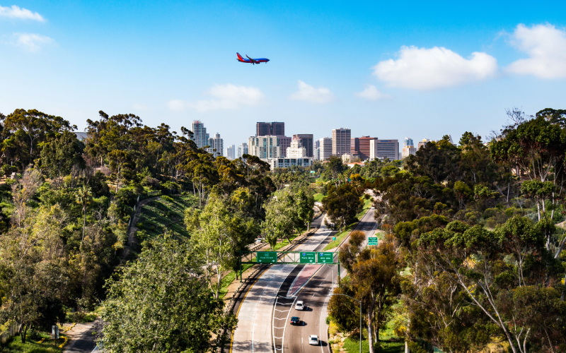 A plane is pictured flying over Downtown San Diego and the State Route 163 freeway through Balboa Park.