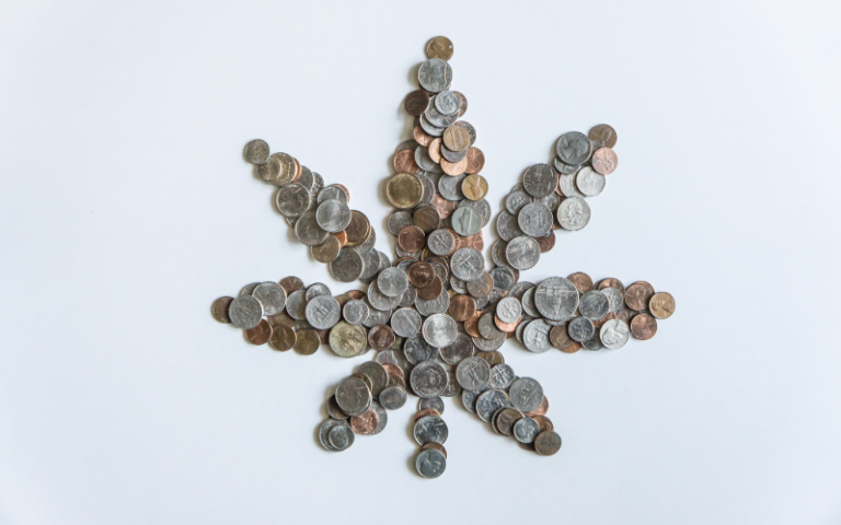 Various coins arranged in the shape of a cannabis leaf on a gray background.